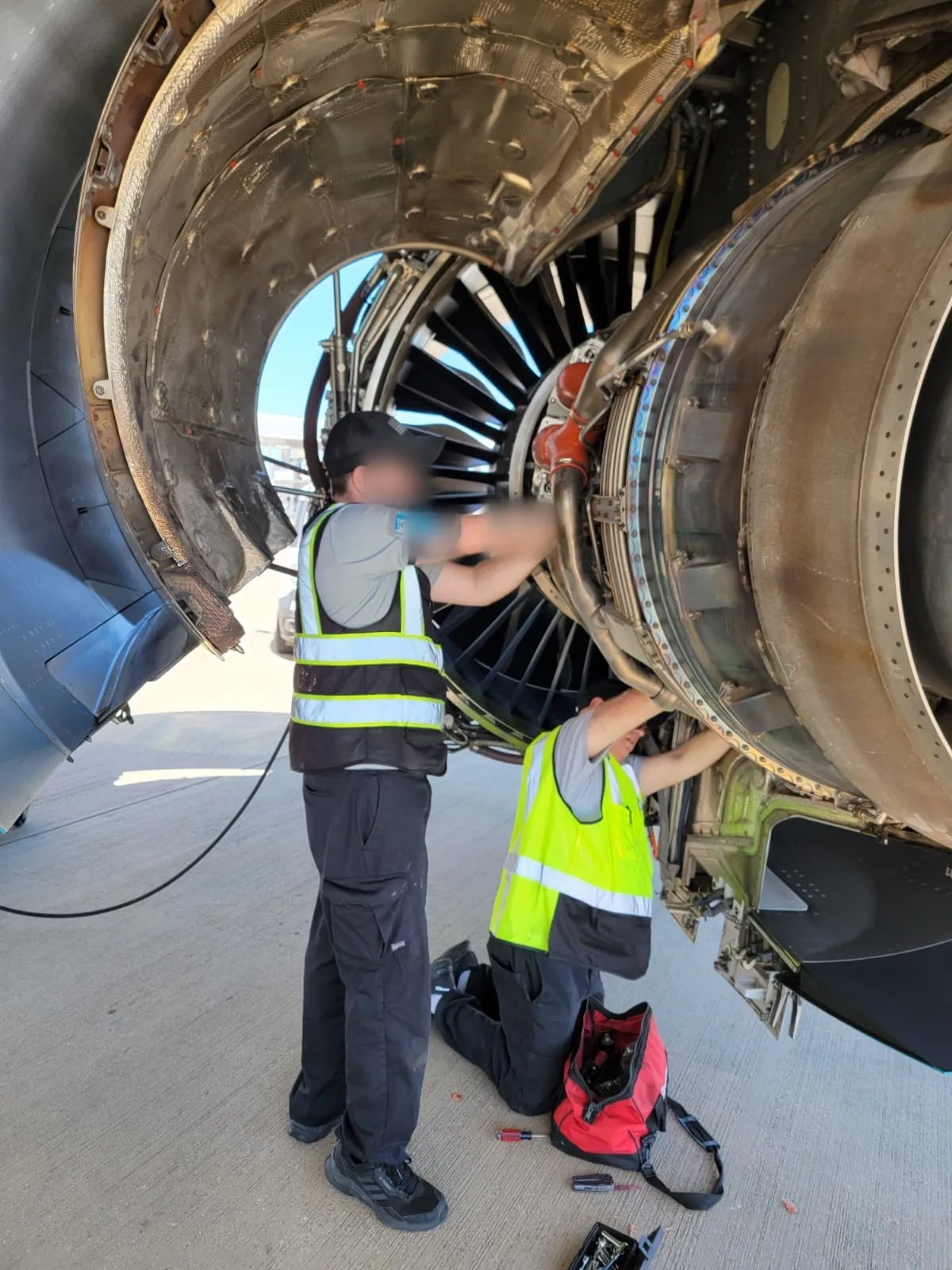 Two mechanics working on an open jet engine fan section